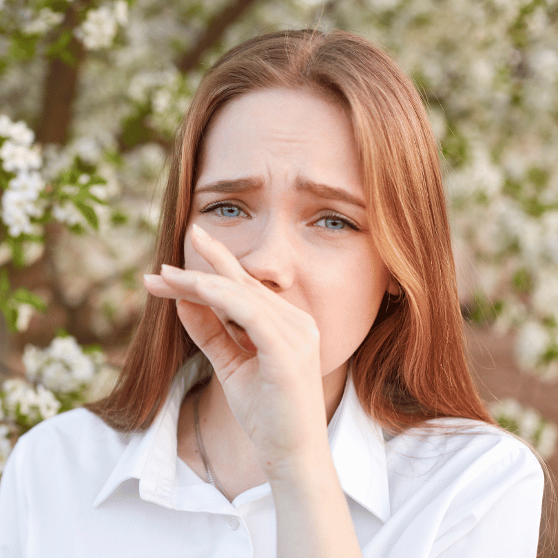 A young woman experiencing allergy symptoms outdoors, highlighting the antiallergic properties of Galangal Root (Alpinia galanga), featured on Zaira Natural.
