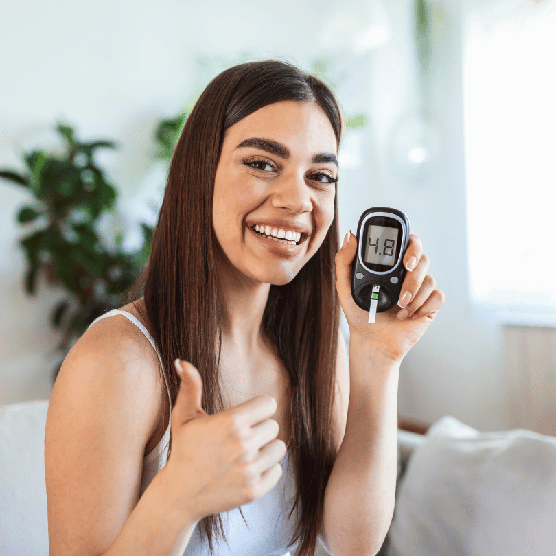 Woman smiling and holding a glucose meter, highlighting the benefits of Zaira Natural’s Swedish Herbs Mix for blood sugar regulation.