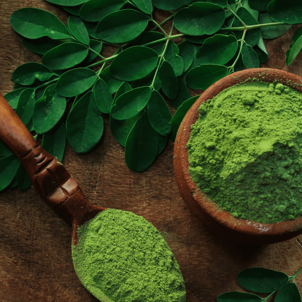 Moringa leaves and powder displayed in a wooden bowl and spoon, representing its antioxidant properties by Zaira Natural