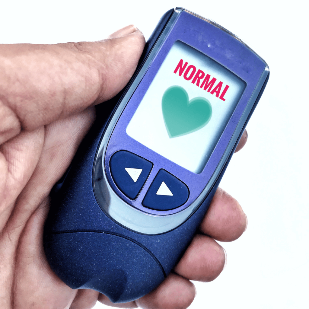 A hand holding a monitor displaying 'normal' blood sugar levels, symbolizing Moringa's role in managing blood sugar by Zaira Natural.